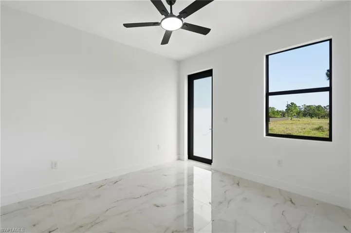 Spacious room featuring large format tile flooring, a black-framed window, a black-framed glass door, and a ceiling fan