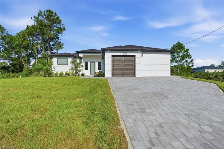 Modern exterior architecture with a flat roofline, gray paver driveway, brown garage door, and a manicured lawn