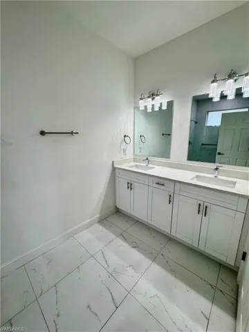 Full bathroom featuring double vanity, light marble finish flooring, and an enclosed shower