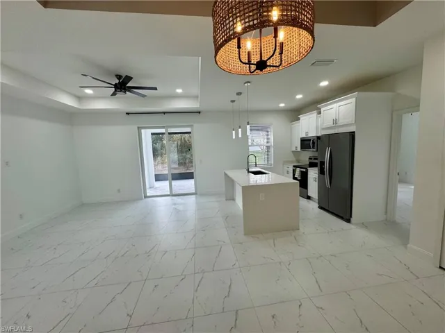 Kitchen featuring a raised ceiling, a chandelier, stainless steel appliances, light marble finish floors, and recessed lighting