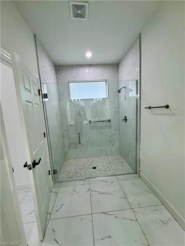 Full bath with light marble finish floors and a marble finish shower