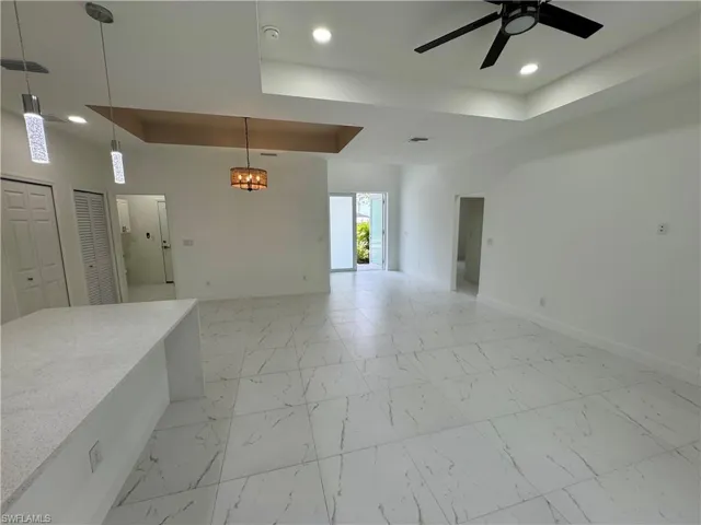 Unfurnished living room featuring a tray ceiling, light marble finish flooring, a chandelier, and ceiling fan