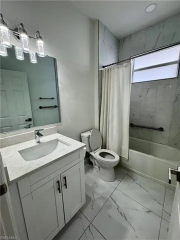 Bathroom with vanity, shower / tub combo with curtain, light marble finish floors, and a textured wall