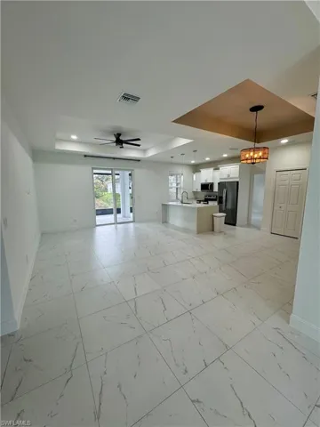 Unfurnished living room with a raised ceiling, light marble finish flooring, a chandelier, and ceiling fan