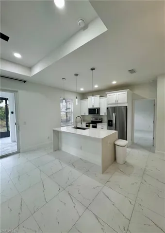 Kitchen featuring light stone counters, pendant lighting, white cabinets, stainless steel appliances, and light marble finish floors