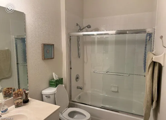 Full bathroom featuring enclosed tub / shower combo, vanity, and a textured wall