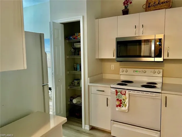 Kitchen featuring white appliances, light countertops, white cabinets, and light wood finished floors