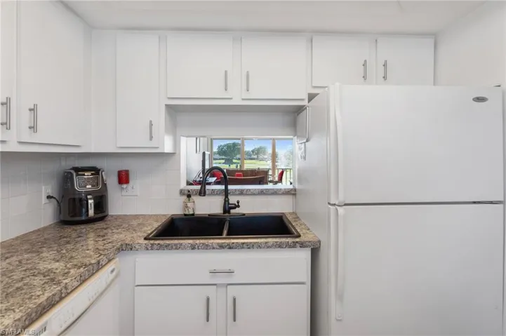 Kitchen with white appliances, backsplash, white cabinetry, and sink