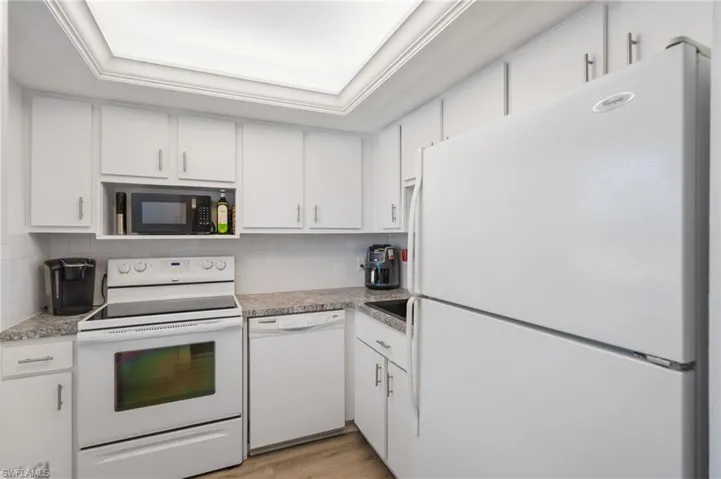Kitchen with white appliances, a tray ceiling, white cabinetry, and tasteful backsplash
