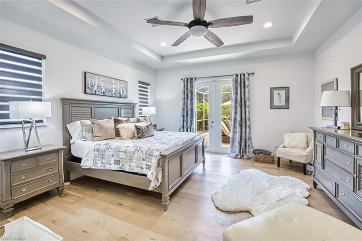 Bedroom with french doors, access to outside, a raised ceiling, light wood finished floors, and recessed lighting