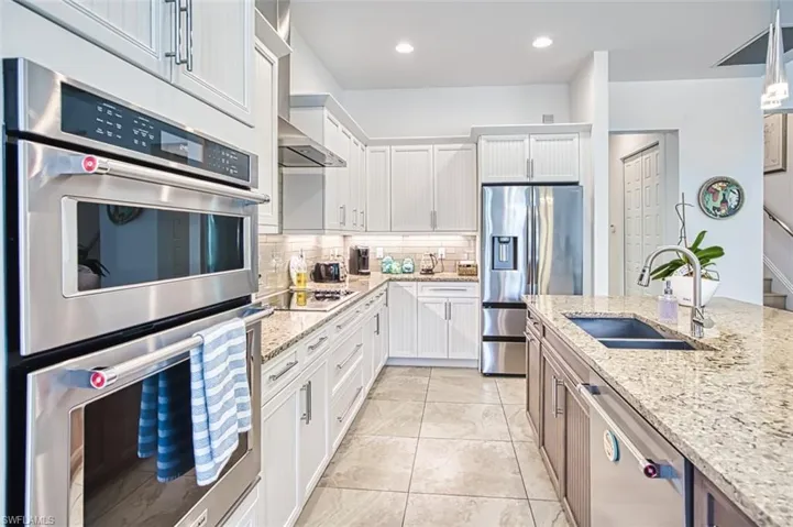 Kitchen featuring stainless steel appliances, tasteful backsplash, white cabinets, light stone counters, and recessed lighting