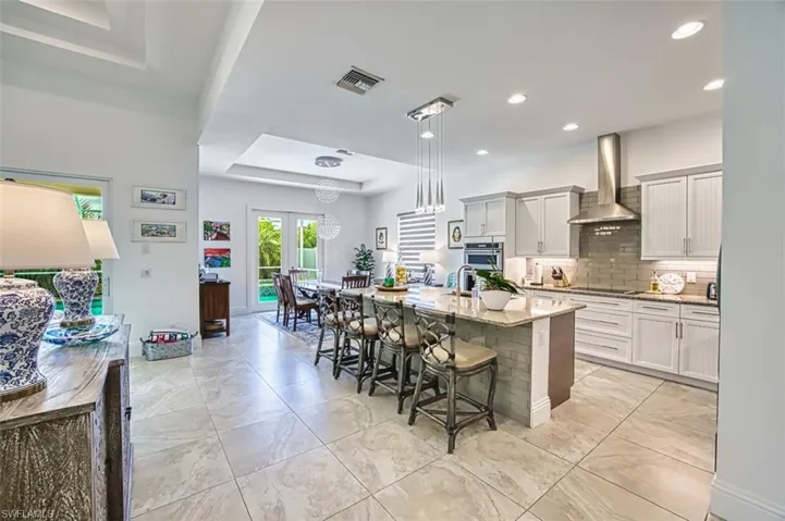 Kitchen featuring a raised ceiling, backsplash, wall chimney exhaust hood, a kitchen breakfast bar, and light stone counters