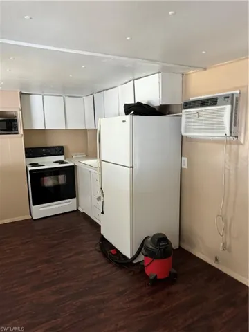 Kitchen with white refrigerator, white cabinets, dark wood-type flooring, and range