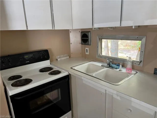 Kitchen with white electric stove, white cabinets, and sink