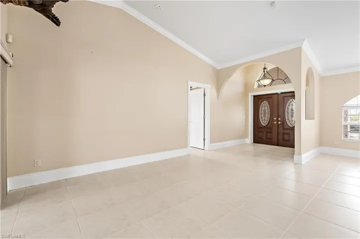 Foyer with ornamental molding, arched walkways, light tile patterned floors, high vaulted ceiling, and french doors