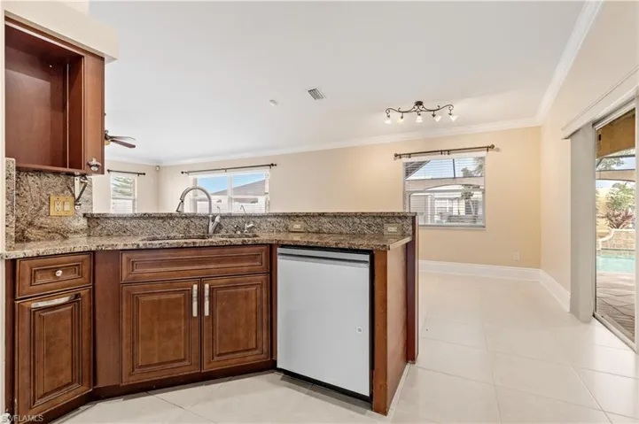 Kitchen featuring stainless steel dishwasher, light stone countertops, crown molding, a peninsula, and brown cabinetry
