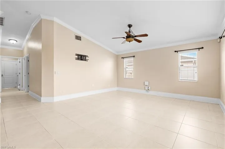 Spare room featuring vaulted ceiling, crown molding, healthy amount of natural light, light tile patterned floors, and a ceiling fan