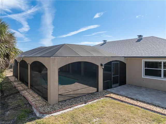 Back of house featuring a sunroom, a shingled roof, glass enclosure, stucco siding, and an outdoor pool