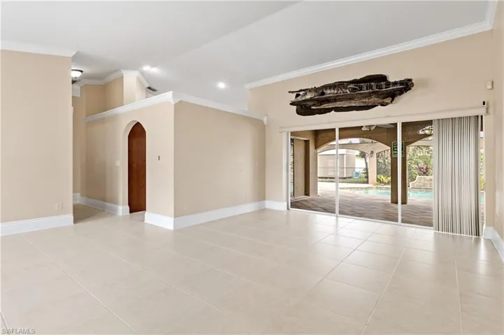 Empty room featuring arched walkways, crown molding, light tile patterned floors, and lofted ceiling