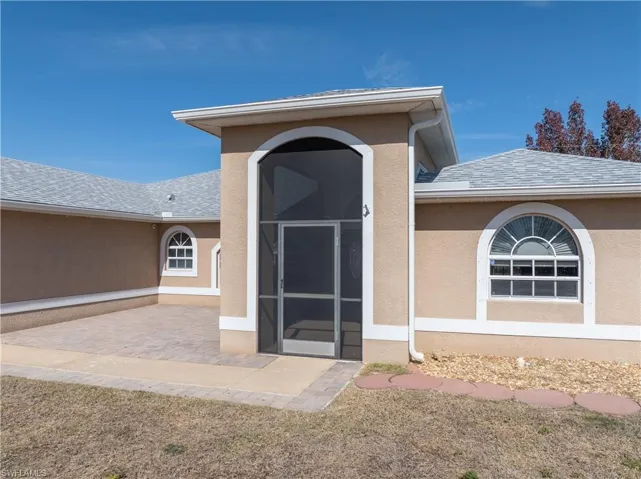 View of exterior entry featuring stucco siding, a sunroom, and a shingled roof