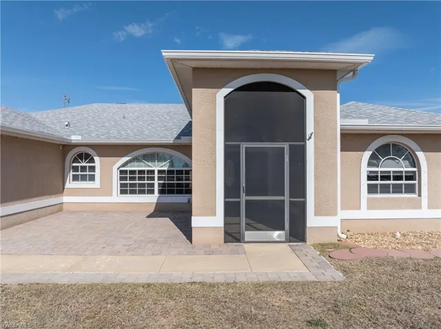 Entrance to property featuring roof with shingles, stucco siding, and a sunroom