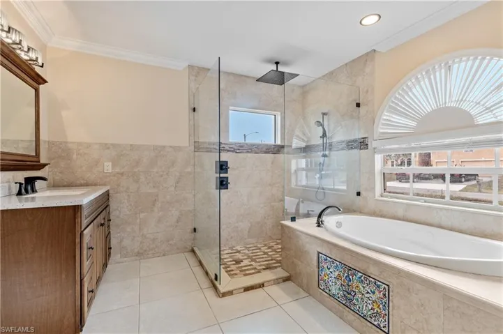 Primary Bathroom featuring a bath, vanity, a stall shower, light tile patterned floors, and tile walls