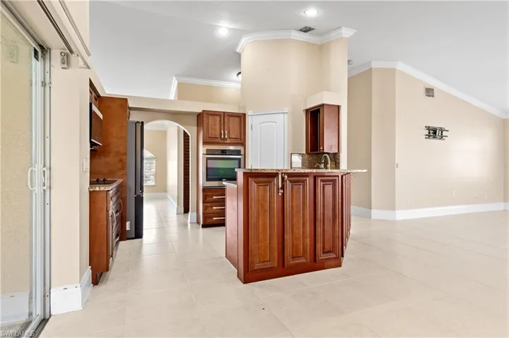 Kitchen with arched walkways, light stone counters, crown molding, light tile patterned floors, and stainless steel oven
