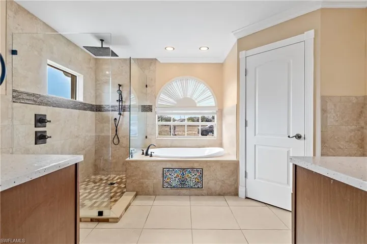 Primary bath with healthy amount of natural light, a garden tub, vanity, walk in shower, and ornamental molding