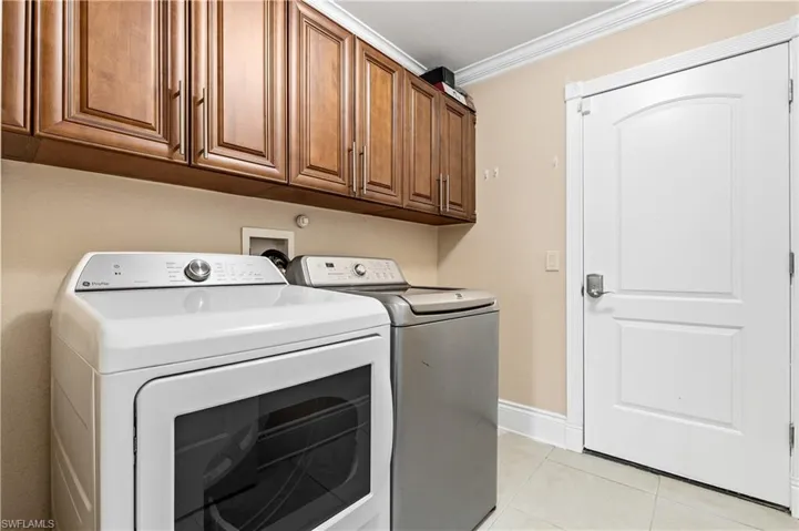 Laundry room with washing machine and clothes dryer, cabinet space, crown molding, and light tile patterned flooring