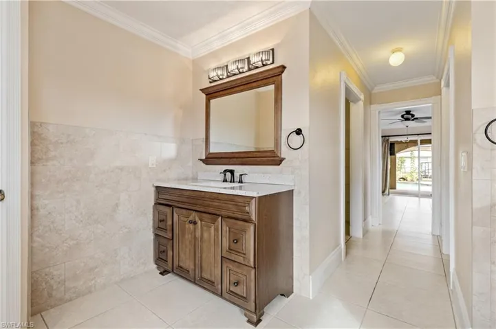 Primary Bathroom featuring ornamental molding, tile walls, vanity, ceiling fan, and light tile patterned floors