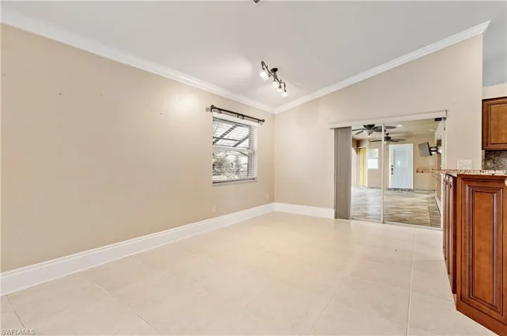 Empty room with vaulted ceiling, ornamental molding, light tile patterned floors, rail lighting, and ceiling fan