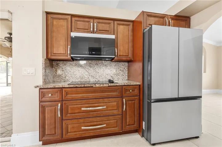 Kitchen featuring arched walkways, appliances with stainless steel finishes, brown cabinetry, and light stone counters