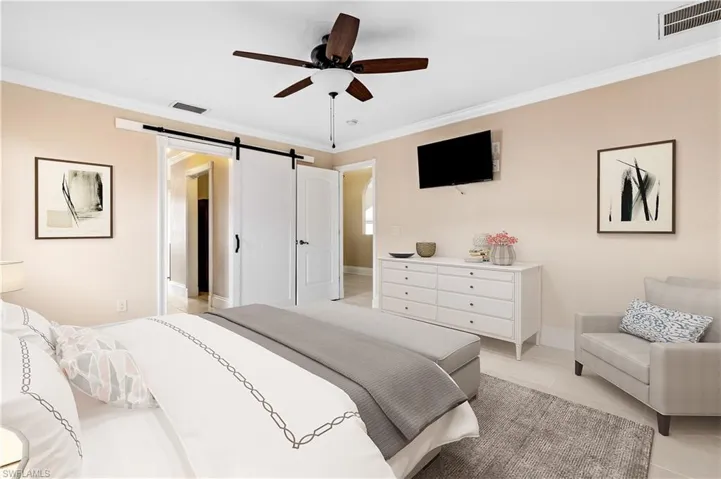 Primary Bedroom with a barn door, ornamental molding, ceiling fan, and light tile patterned floors