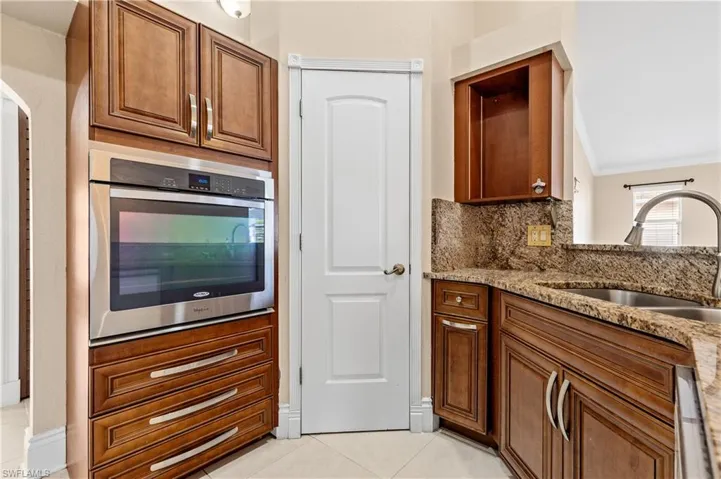 Kitchen featuring brown cabinetry, oven, light stone countertops, light tile patterned floors, and decorative backsplash