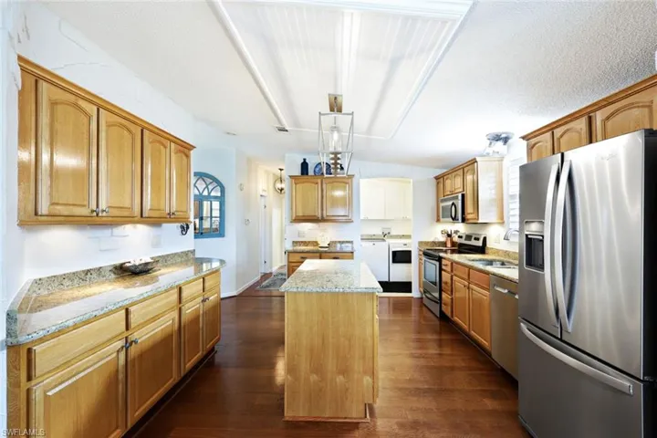 Kitchen featuring light stone counters, stainless steel appliances, dark wood-type flooring, pendant lighting, and a kitchen island