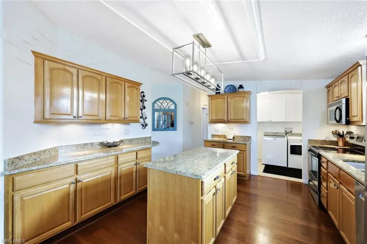 Kitchen with pendant lighting, a textured ceiling, appliances with stainless steel finishes, a kitchen island, and washing machine and clothes dryer