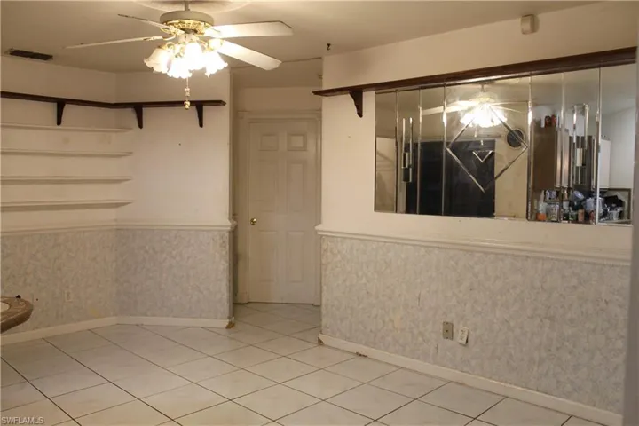 Spare room featuring ceiling fan, a wainscoted wall, wallpapered walls, and light tile patterned flooring