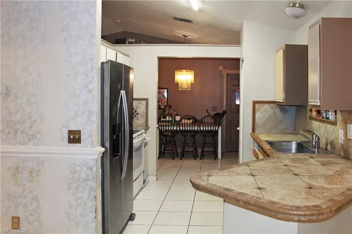 Kitchen with stainless steel refrigerator with ice dispenser, vaulted ceiling, decorative light fixtures, a chandelier, and light tile patterned floors
