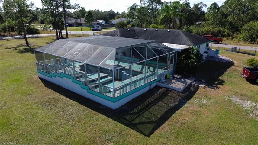 Back of property with a yard, glass enclosure, a jacuzzi, and an outdoor pool