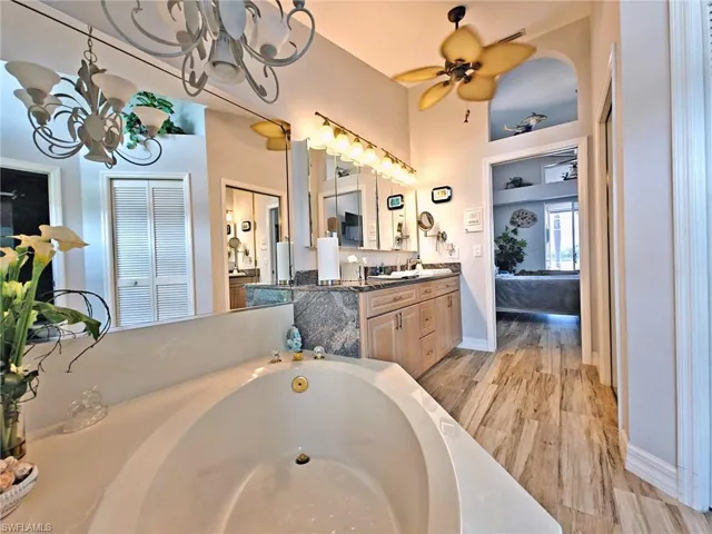 Full bathroom with a washtub, ceiling fan with notable chandelier, ensuite bathroom, wood finished floors, and vanity