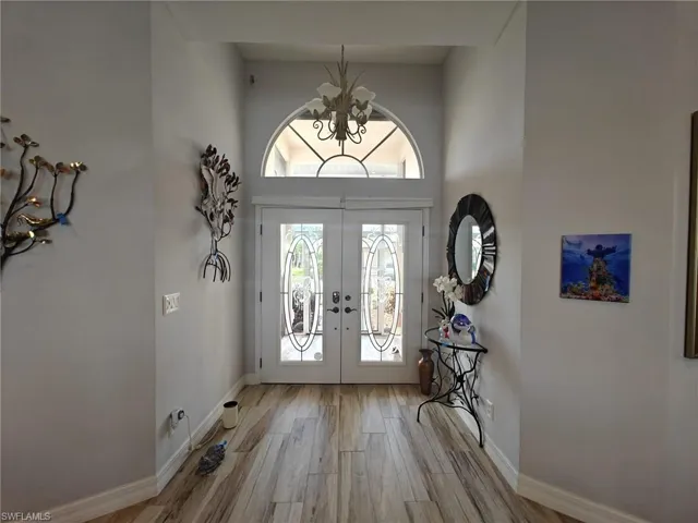 Entryway with a notable chandelier, french doors, baseboards, and light wood-style floors