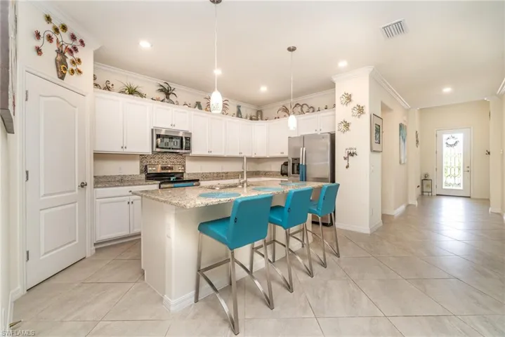 Kitchen featuring white cabinetry, tasteful backsplash, an island with sink, light stone counters, and appliances with stainless steel finishes