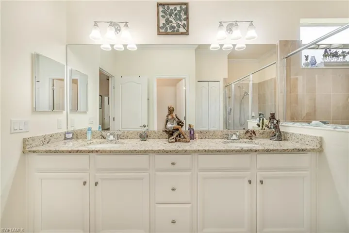 Bathroom with dual vanity, a shower with door, and crown molding