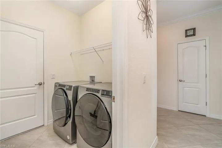 Laundry room featuring washer and dryer, light tile patterned floors, and crown molding