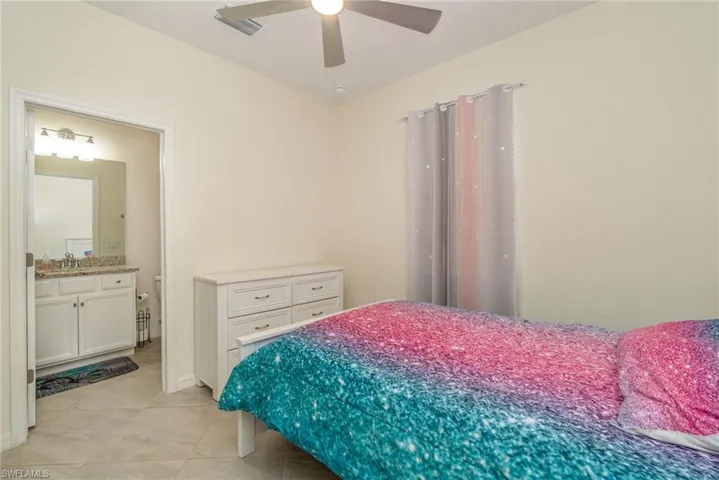 Bedroom featuring connected bathroom, light tile patterned floors, and ceiling fan