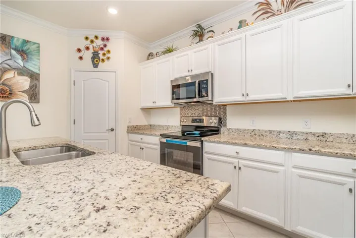 Kitchen with appliances with stainless steel finishes, sink, light tile patterned floors, crown molding, and white cabinetry