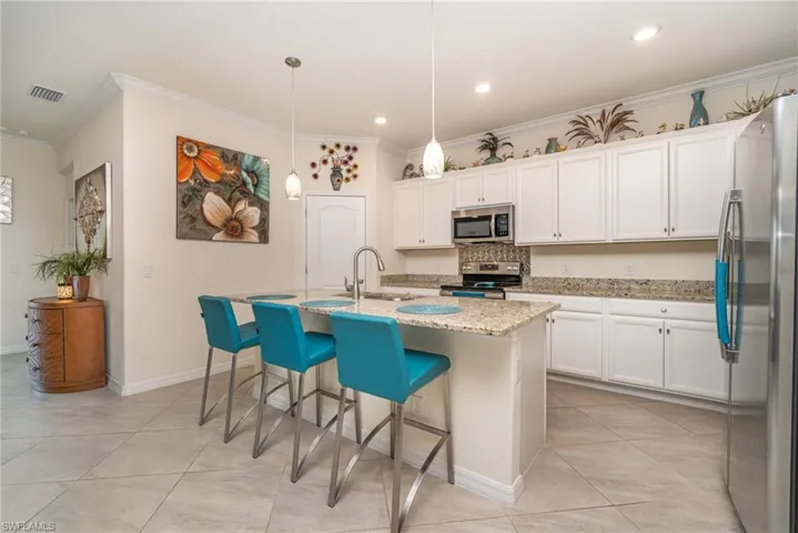 Kitchen featuring stainless steel appliances, decorative light fixtures, light stone countertops, and an island with sink