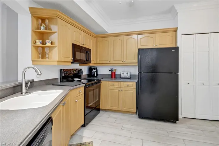 Kitchen featuring light brown cabinetry, sink, black appliances, and ornamental molding