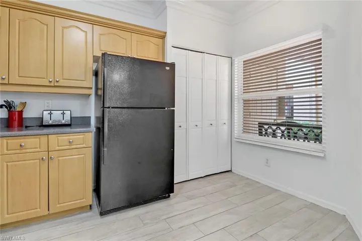 Kitchen featuring light brown cabinetry, ornamental molding, and black refrigerator