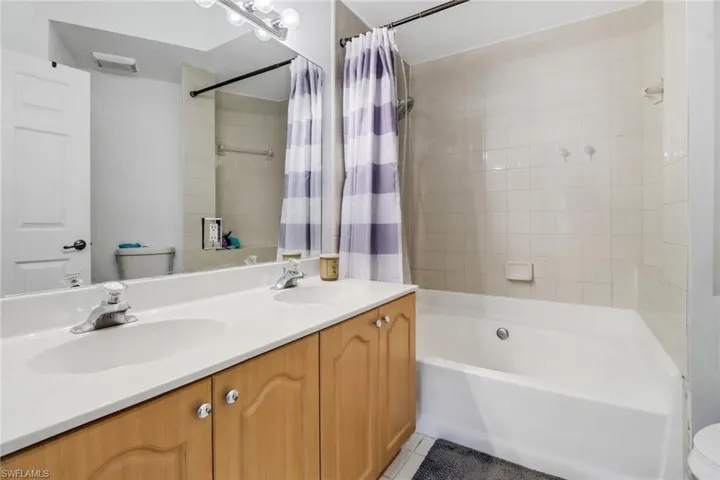 Full bathroom with tile patterned floors, shower / bath combo with shower curtain, double sink vanity, and toilet